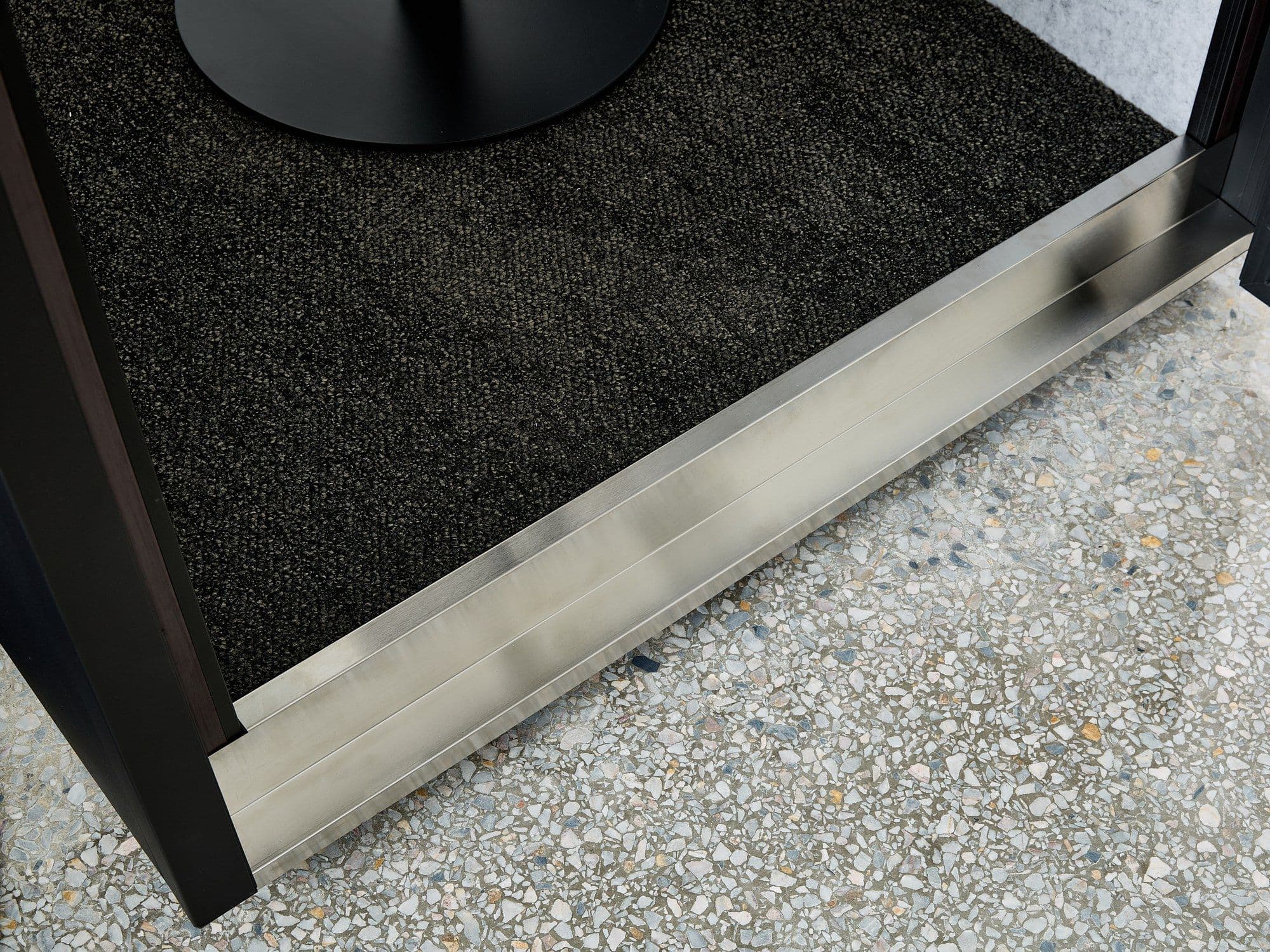 The brushed stainless threshold strip at the base of a Peacepod door, where the dark interior carpet meets the floor outside