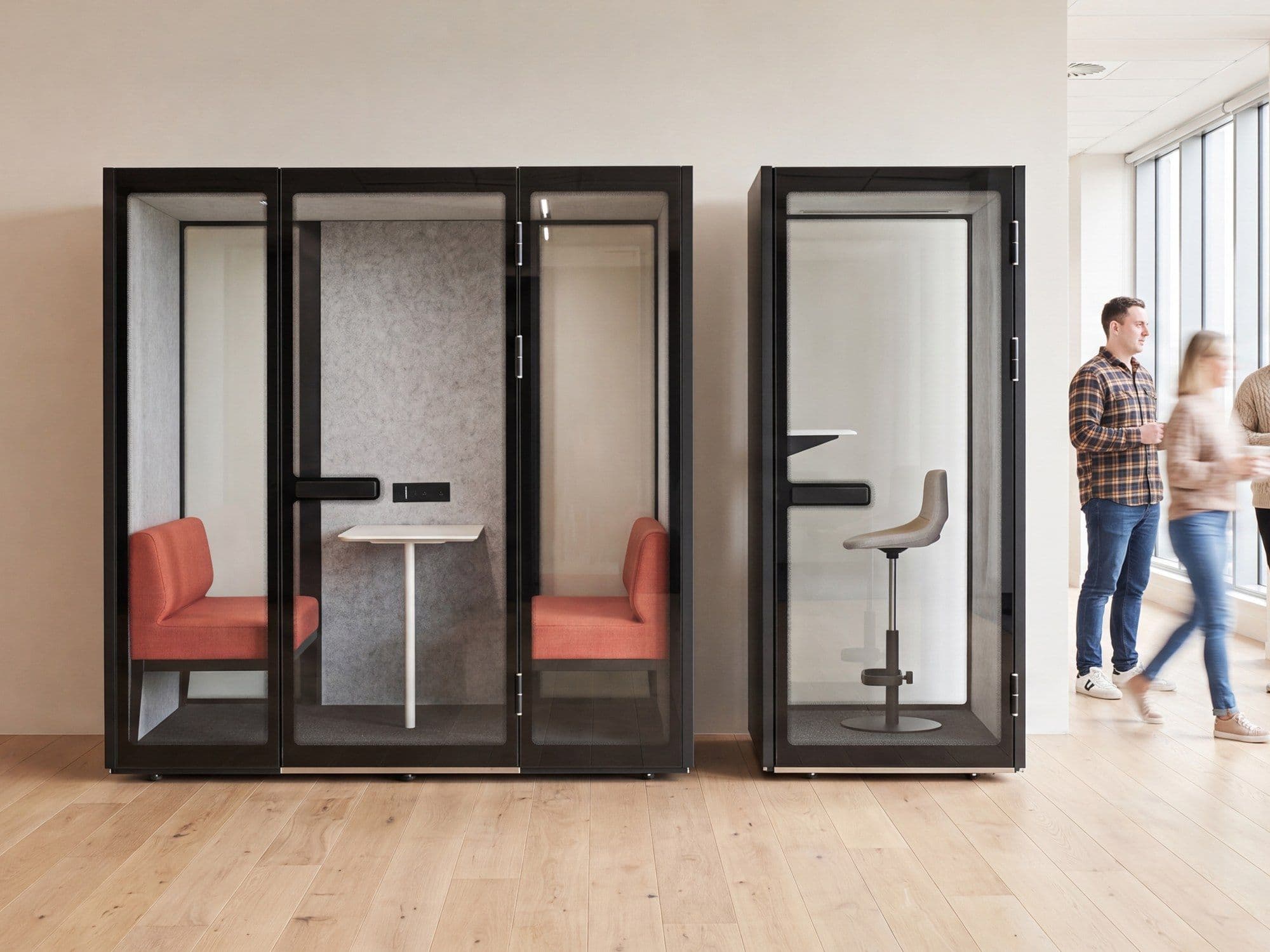 Two Peacepods in an open-plan office, with colleagues walking past