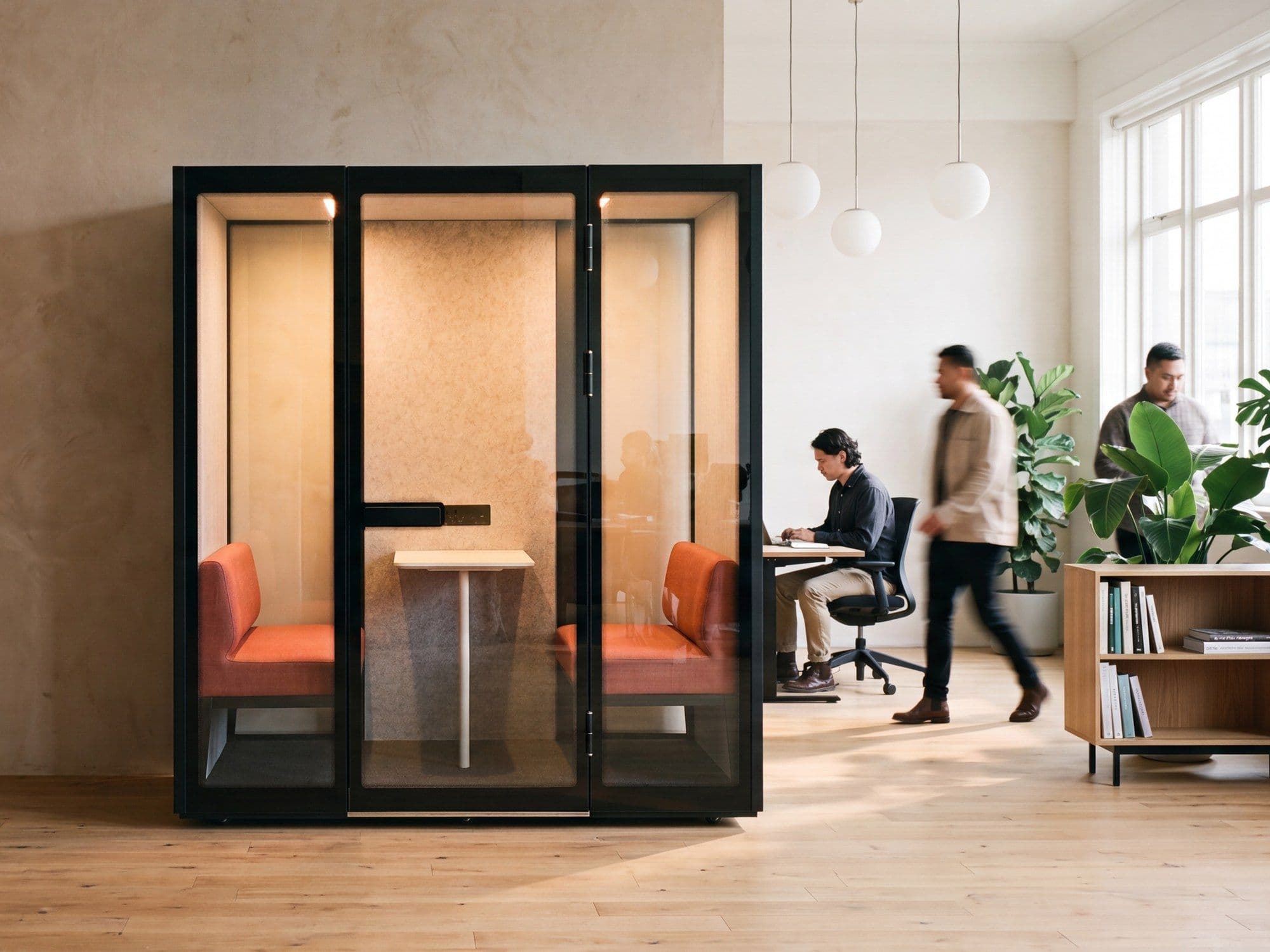 Two Peacepods in an open-plan office, with people working at desks nearby