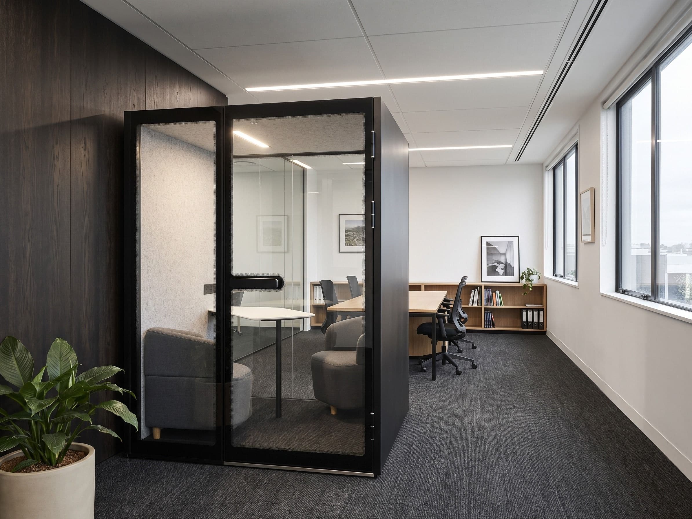 An M2-Pod installed against a dark timber wall in a quiet office, with desks, a bookshelf and windows beyond