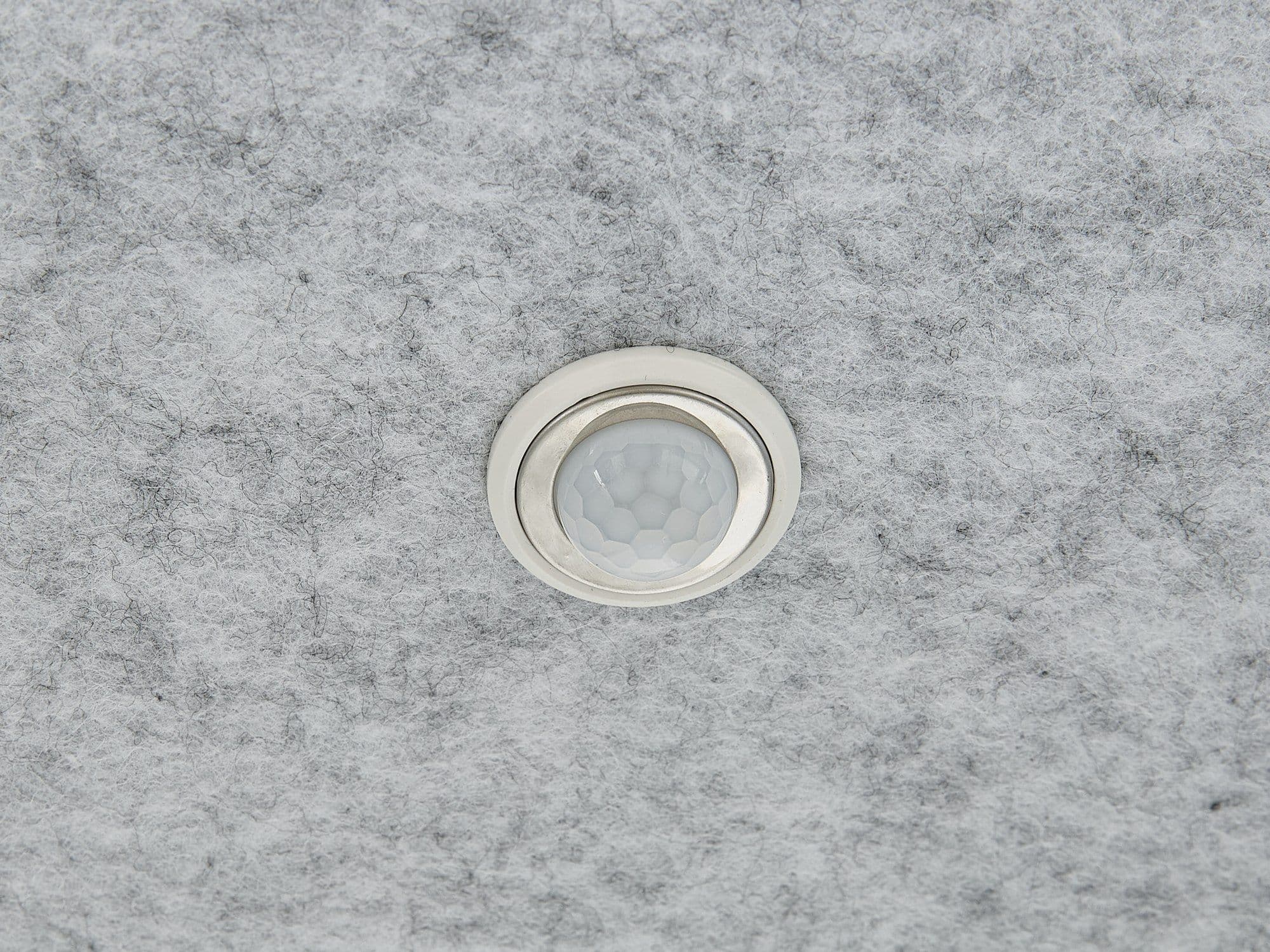 The recessed motion sensor set into the grey acoustic felt ceiling of a Peacepod