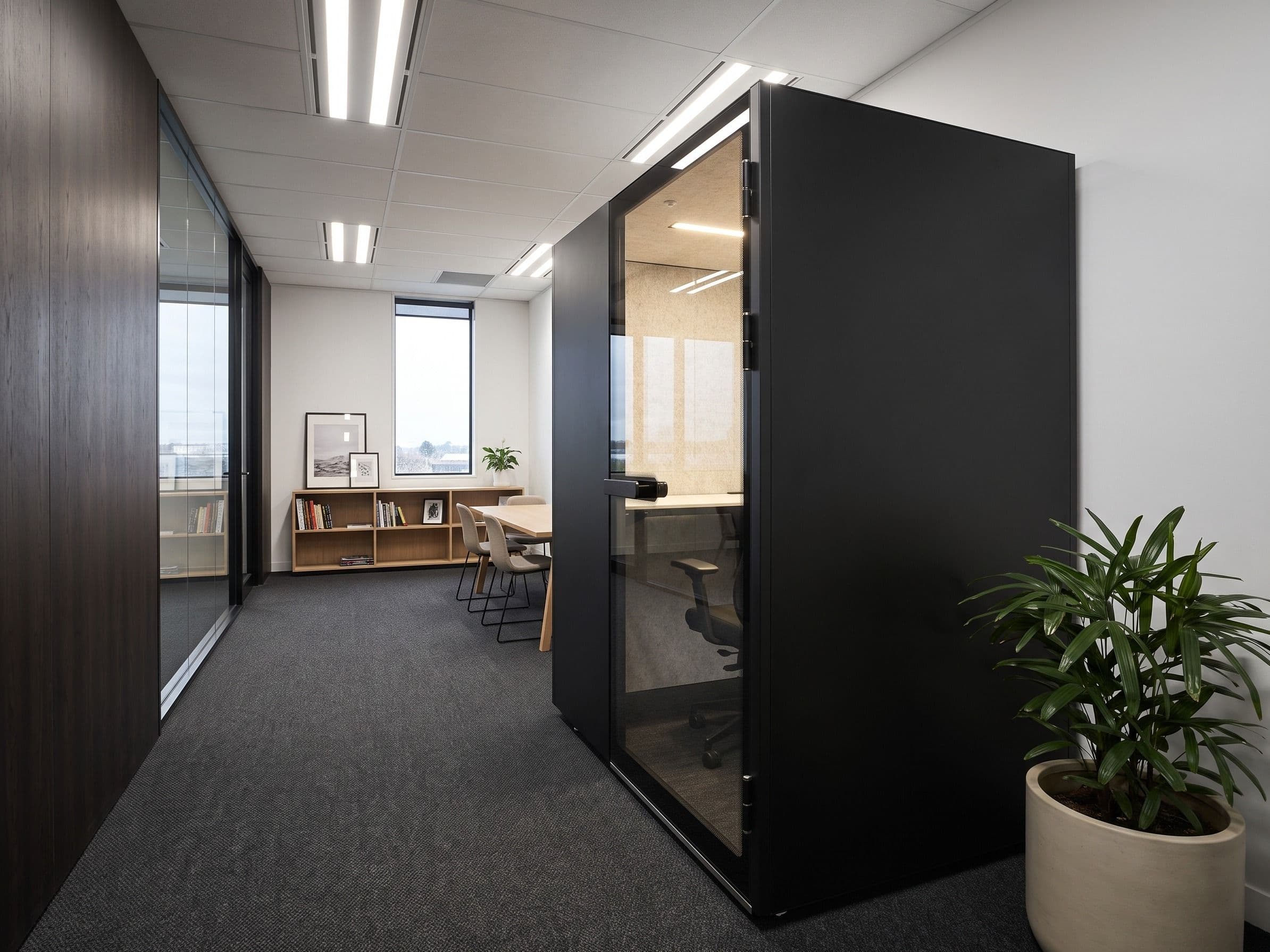 An MW-Pod installed at the end of an office walkway, seen from one side, with a meeting table and shelving beyond